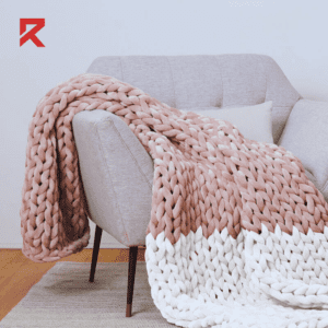 A hand woven blanket in white and pink color on grey sofa chair. Seems like a good gift for women on christmas.